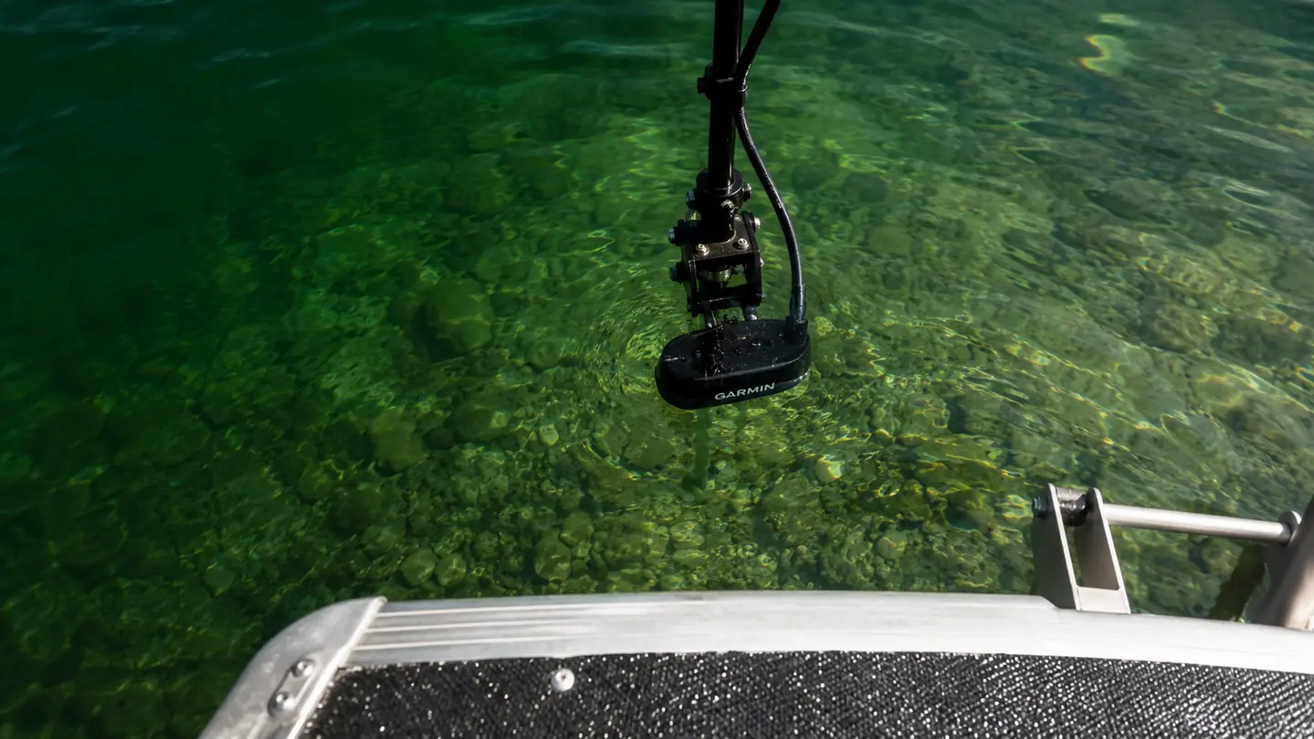 The sonar transducer hanging just below the transom in clear green water.