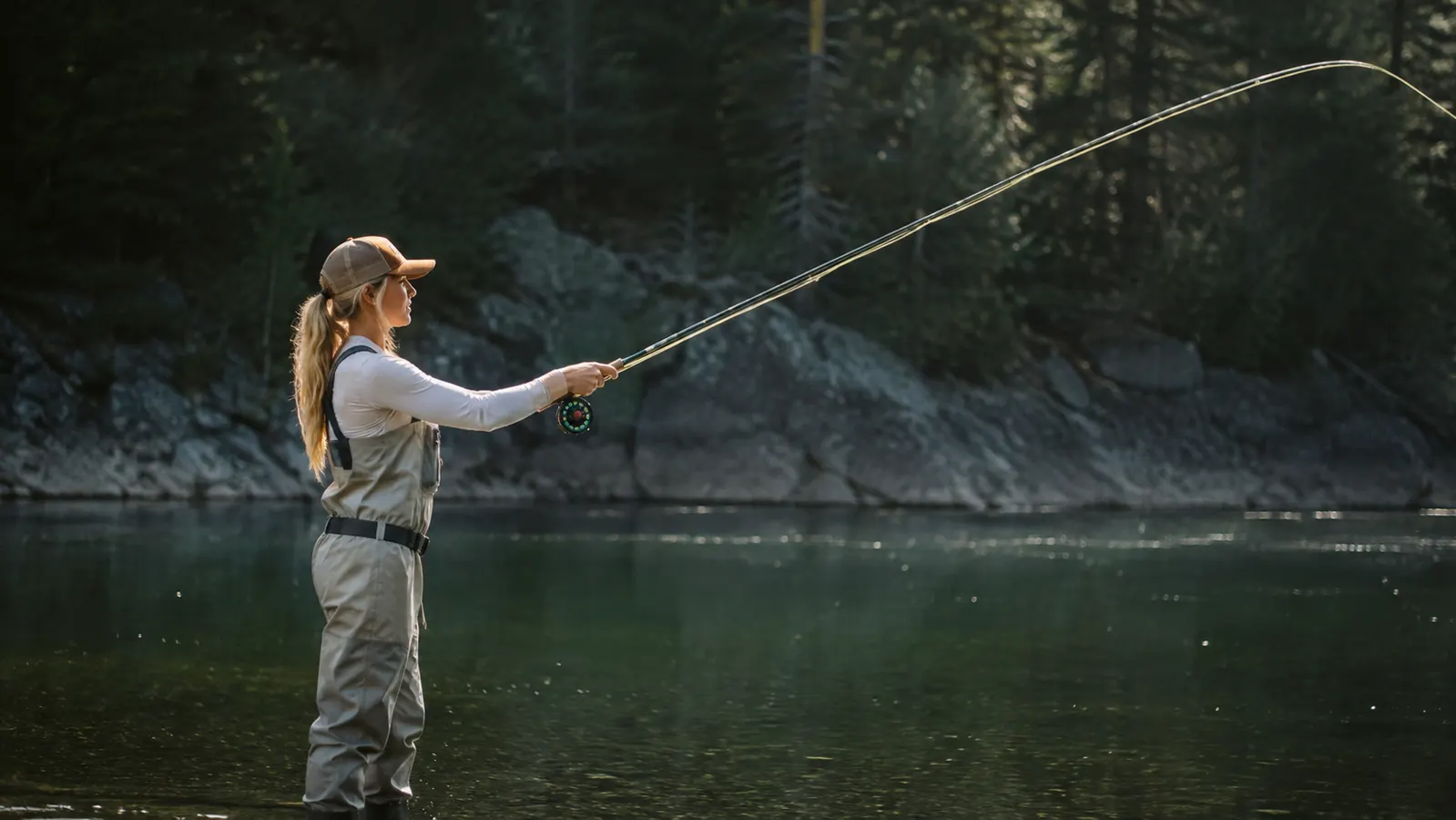 Side view of an angler at the forward stop of a cast, line arcing out over a calm green river pool