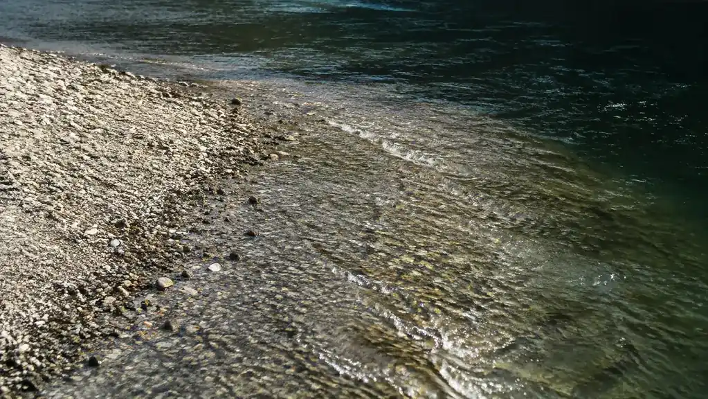 A gravel point sloping into deeper, darker water on a river, where fish hold along the break